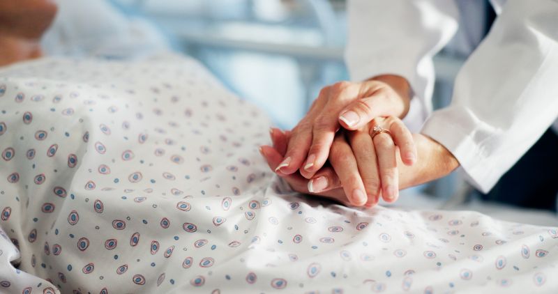 nurse holding patient's hand in palliative care.